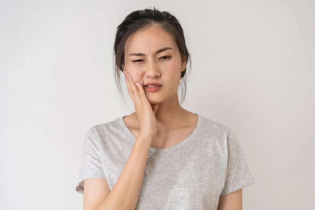 Female patient holding her cheek, experiencing toothache, visiting emergency dentist in Chicago.