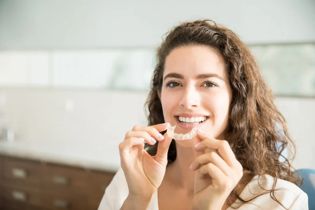 Female patient smiling while holding Invisalign aligners in Chicago.
